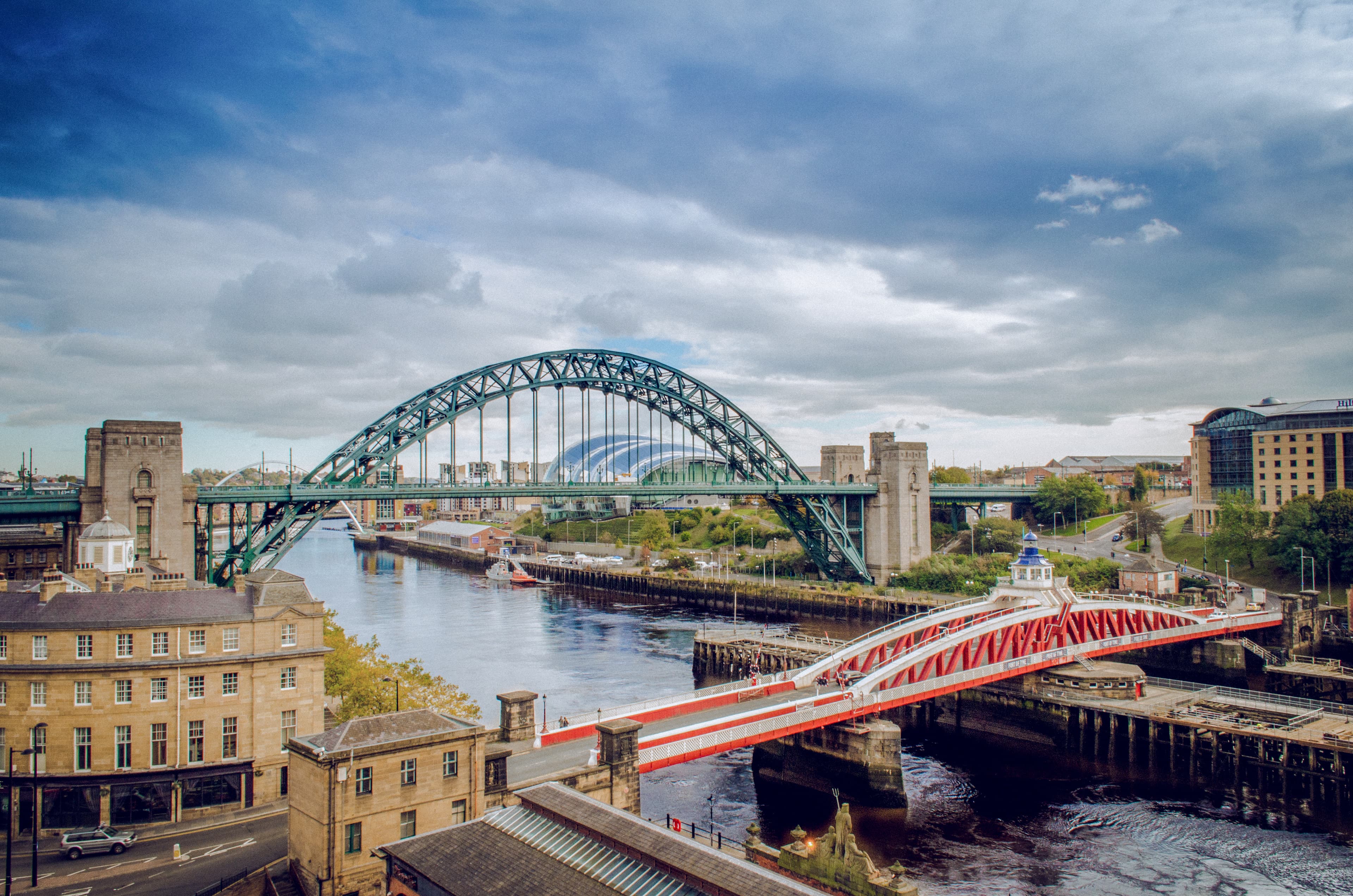 A view of Newcastle upon Tyne, showcasing the iconic Tyne Bridge and Swing Bridge over the River Tyne, with the city’s mix of historic and modern architecture in the background.