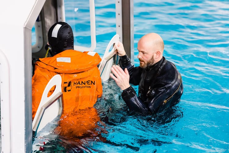 Instructor guiding a trainee through water evacuation procedures, focusing on practical skills for safety and survival in offshore conditions.