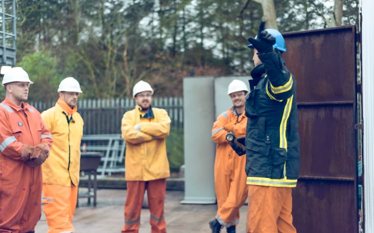 group of workers wearing safety gear, including hard hats and fire-resistant suits, gathered outdoors for a training session.