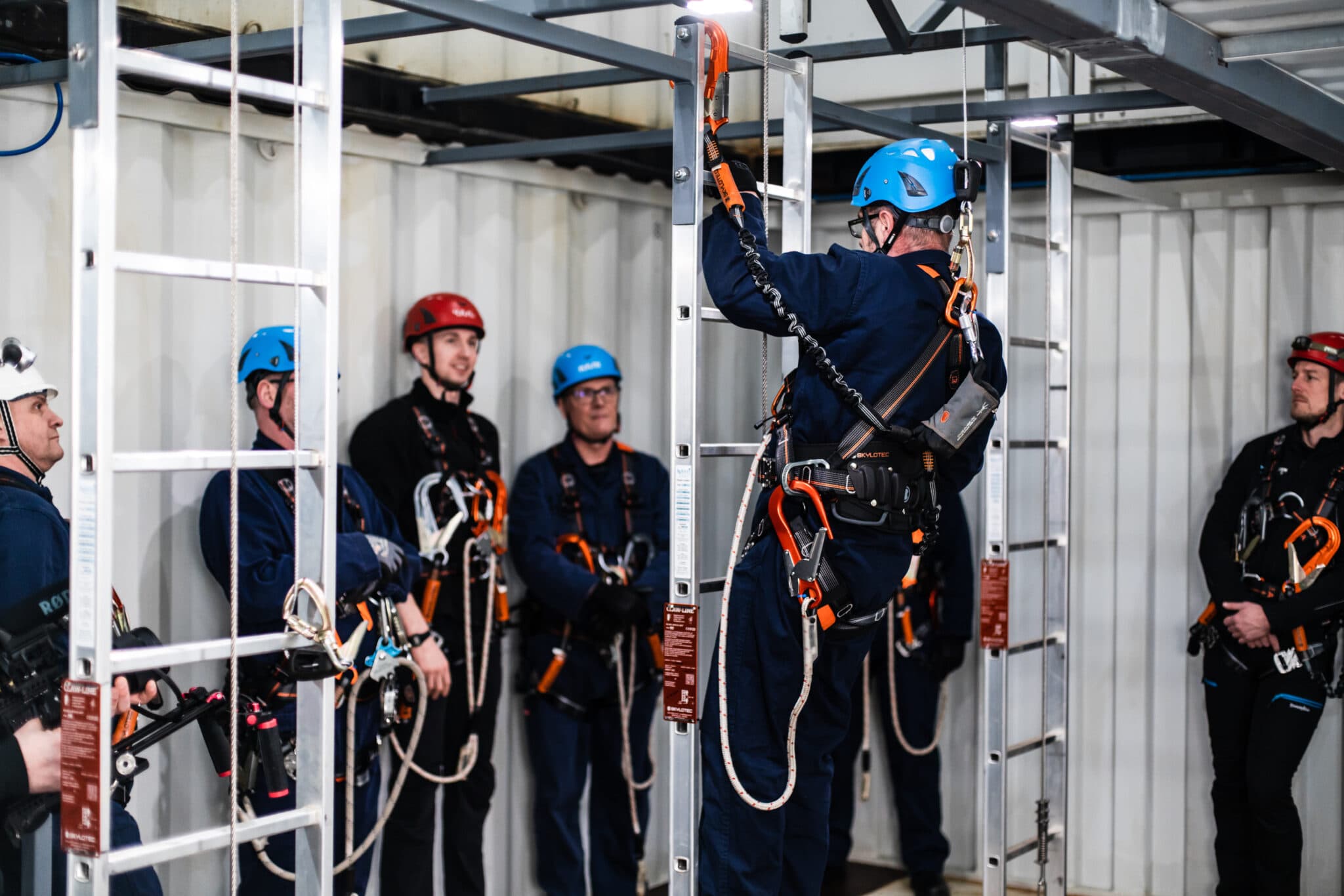 Training session with trainees in safety gear practising ladder climbing and fall protection techniques under the guidance of an instructor.