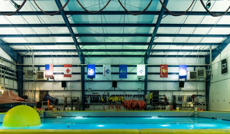 Indoor rescue training facility featuring a large pool, safety equipment, and international flags, designed for simulating maritime and offshore emergency scenarios.