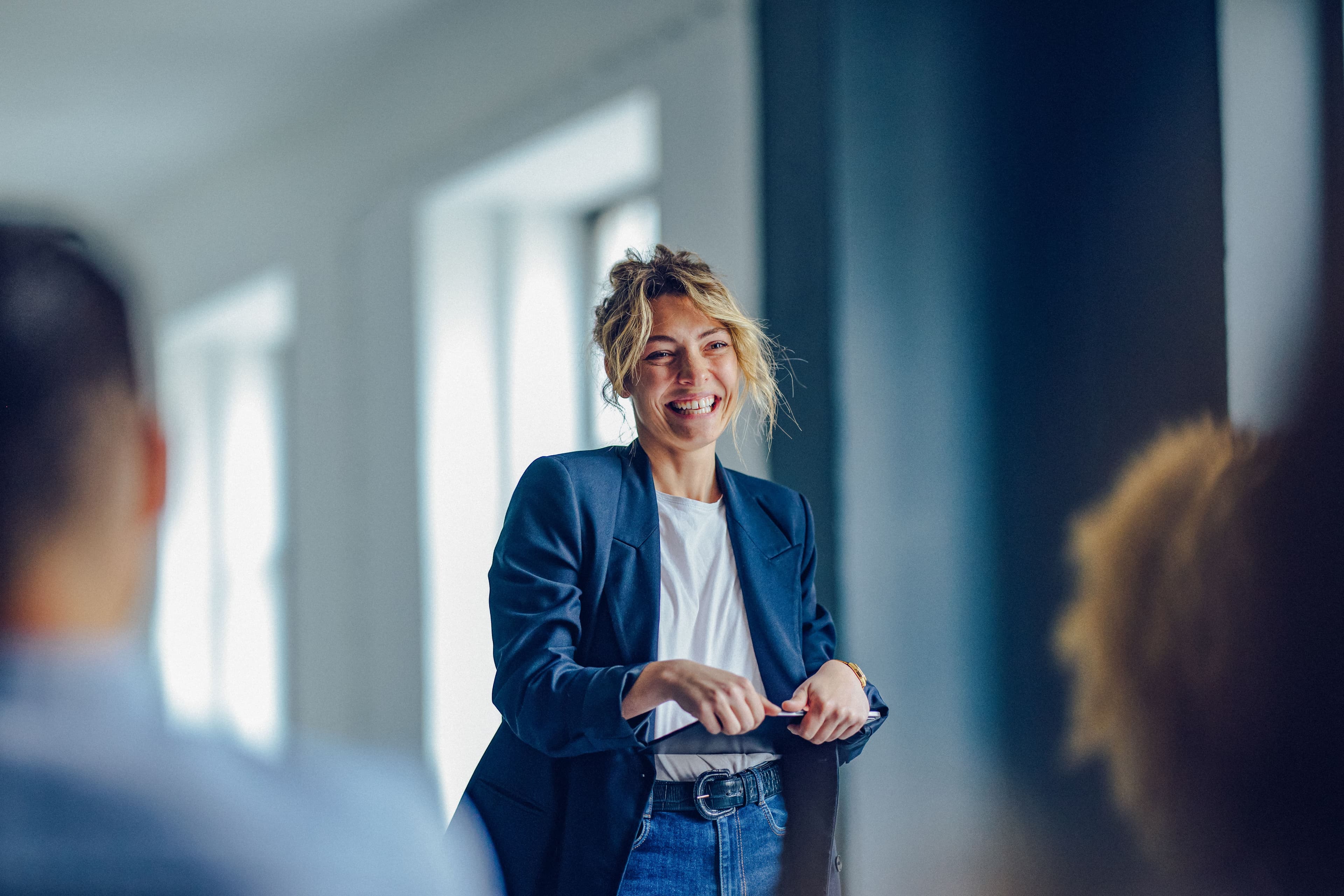 A woman confidently leads a meeting in a bright, modern office setting, engaging with her colleagues in a friendly and professional manner. The atmosphere reflects a positive and collaborative work environment.