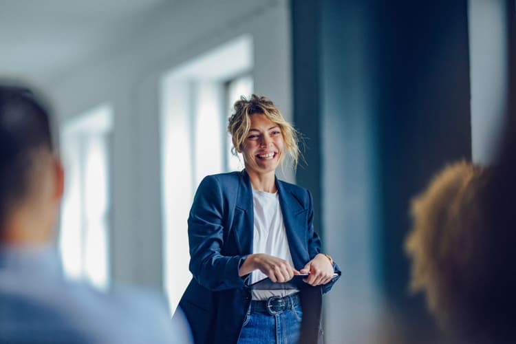 A woman confidently leads a meeting in a bright, modern office setting, engaging with her colleagues in a friendly and professional manner. The atmosphere reflects a positive and collaborative work environment.