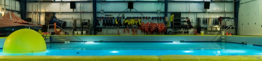 Indoor rescue training facility featuring a large pool, safety equipment, and international flags, designed for simulating oil and gas and offshore emergency scenarios.